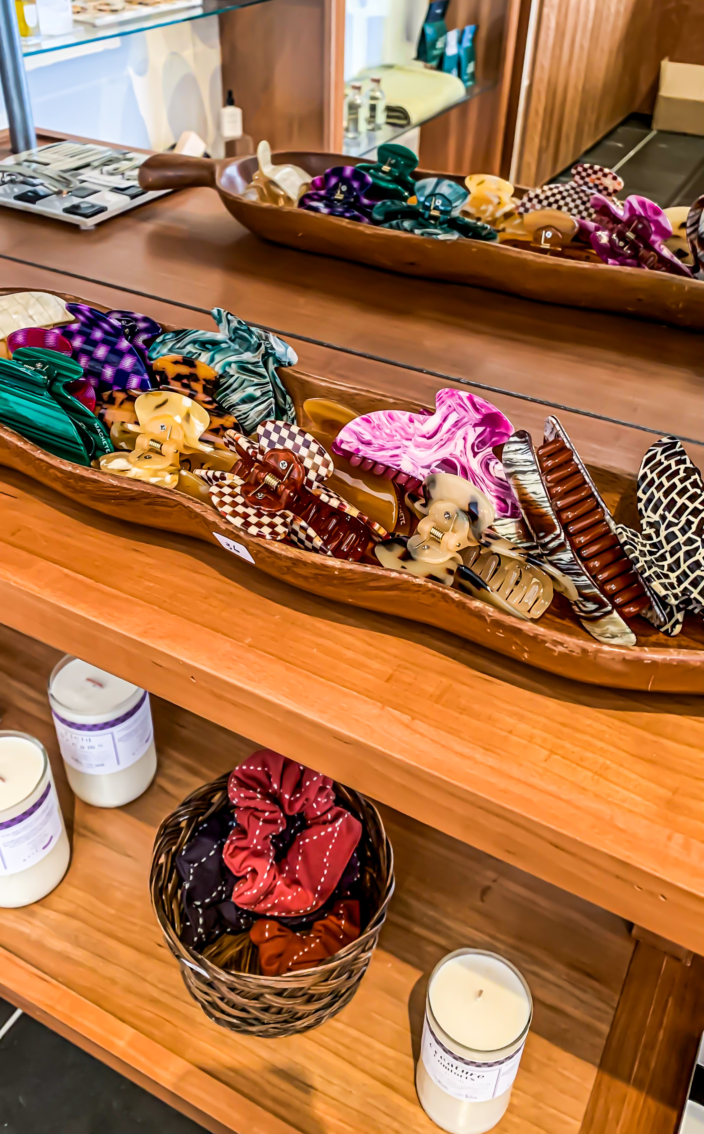 Machete Hair Claw display at Green & Bean boutique in Annapolis maryland. The bottom shelf has a basket of scrunchies and there is a mirror to reflect the wooden container of hair claws