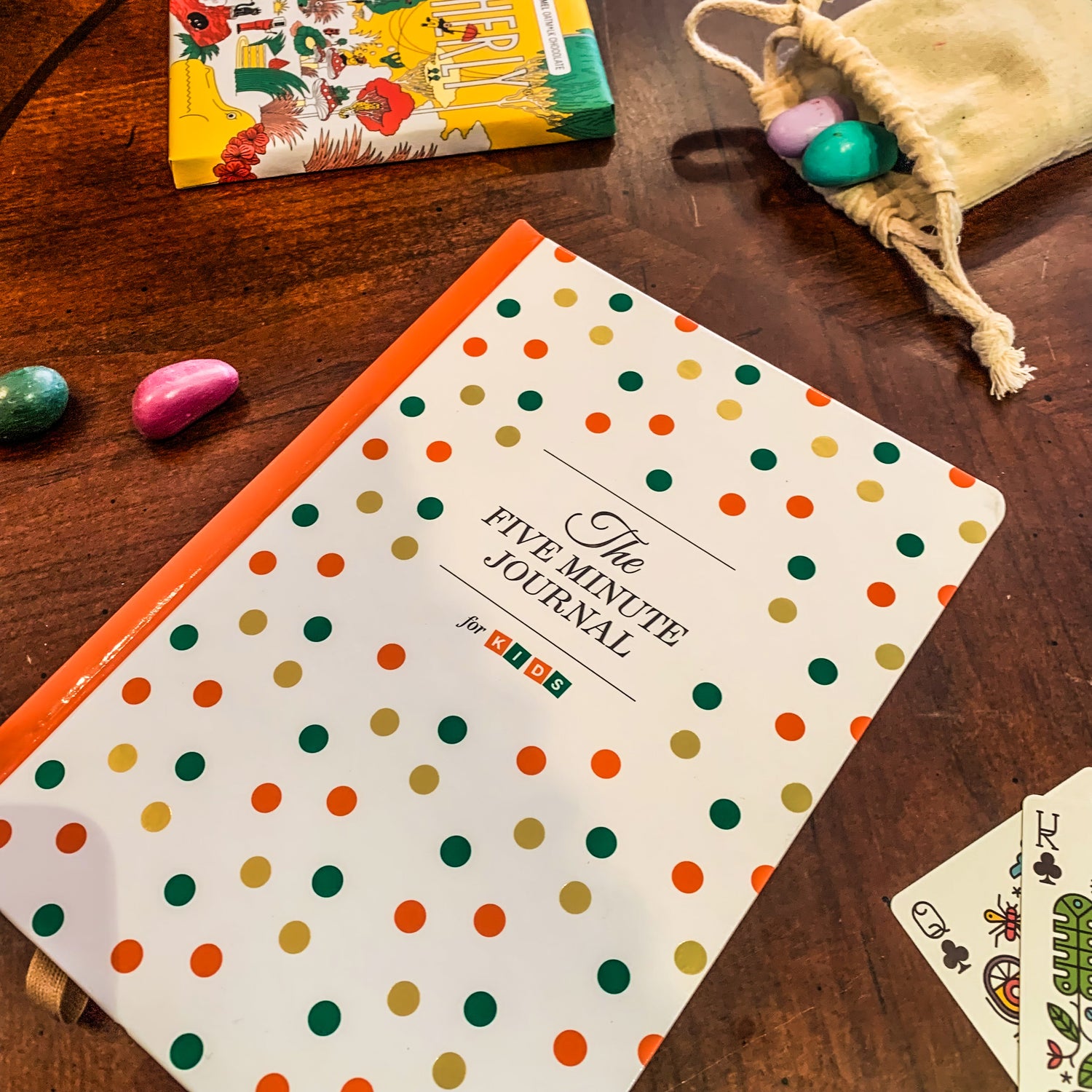 Items from our children's section with Intelligent Change's "Five Minute Journal for Kids" with some crayon rocks, a couple playing cards, and a chocolate bar in the background for context.