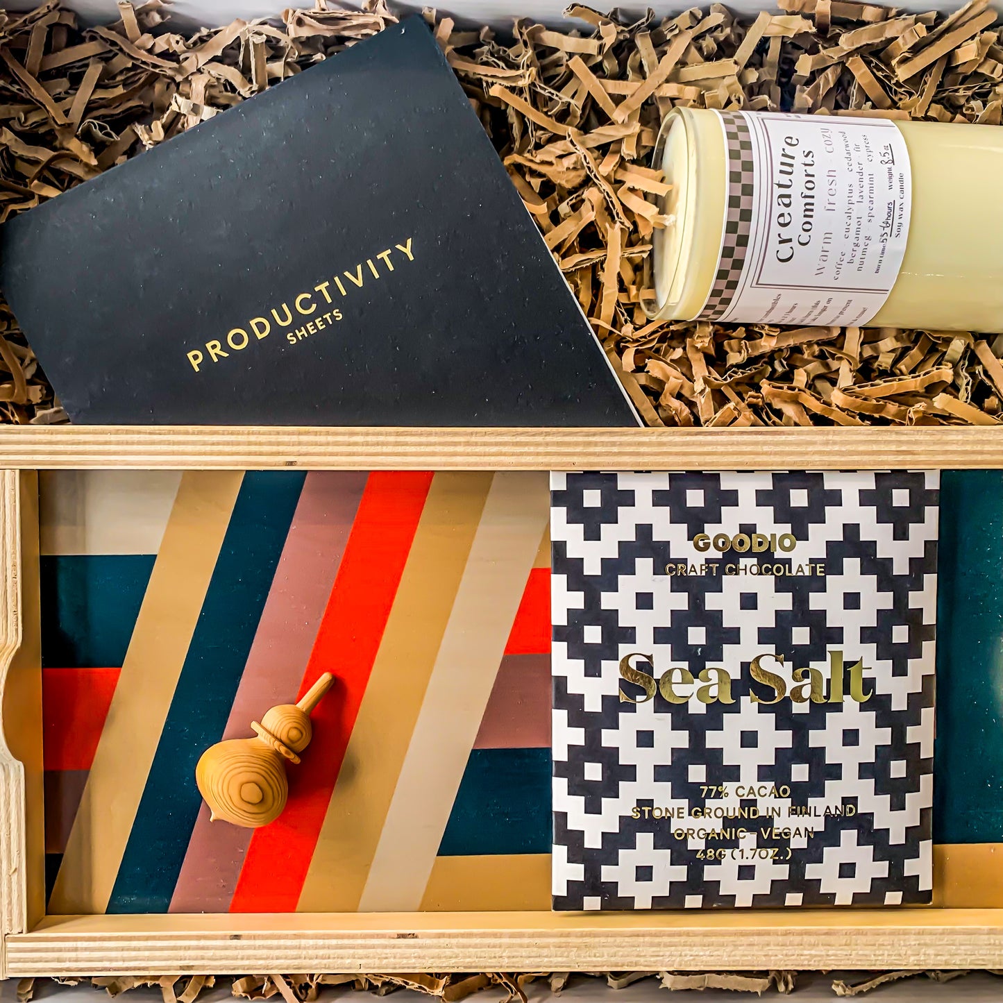 "Home Office" Gift box contains a masculine wooden tray with thick stripes and a red accent. There is a sea salt bar of chocolate, a pack of Productivity Sheets, a wooden spinning top and a soy wax candle