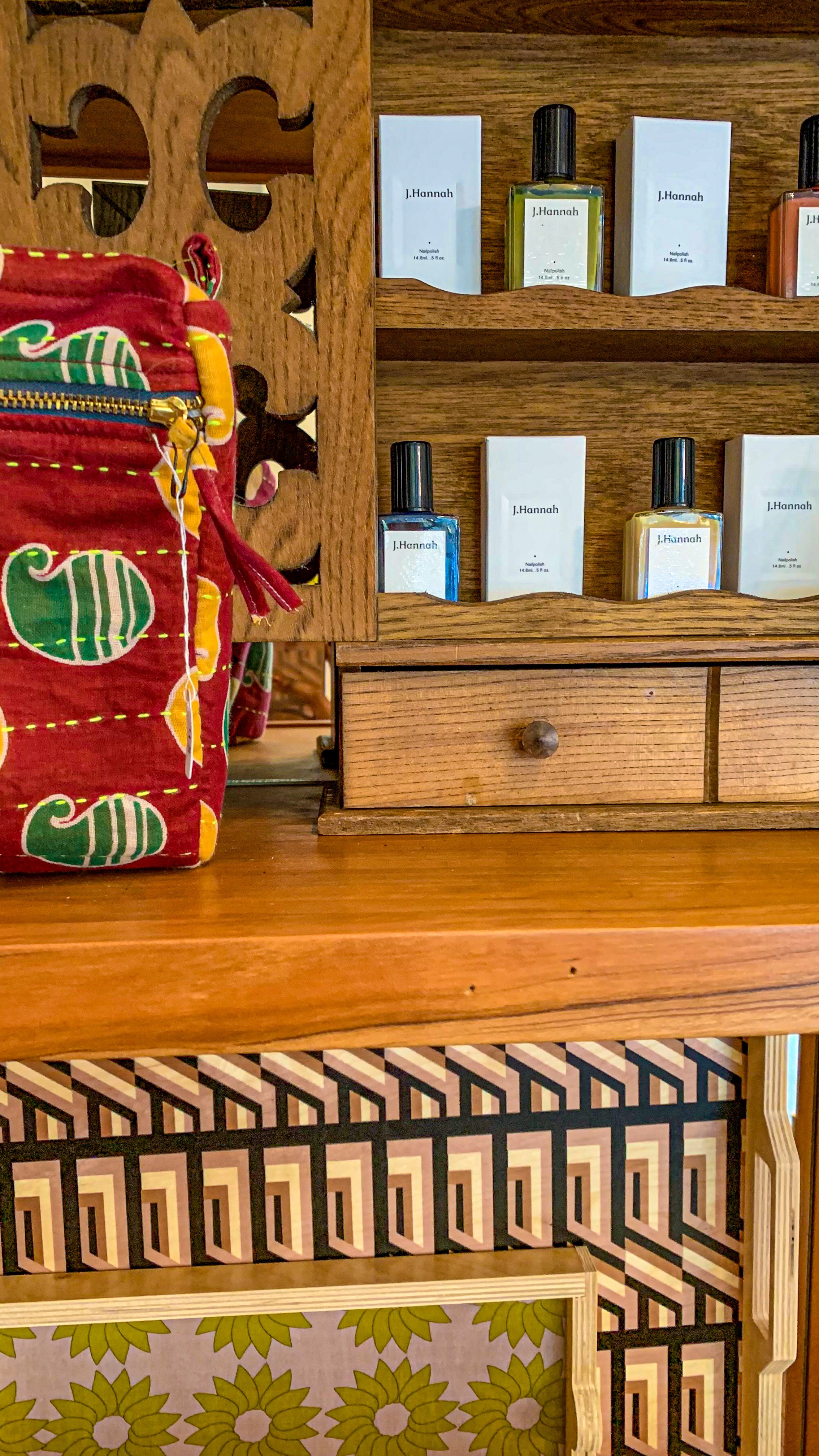 Close-up shelf display with a red vintag kantha toiletry bag in the upper left corner, a wooden display cabinet with nail polishes in the top right corner and the bottom half of the photo are two patterned wood trays