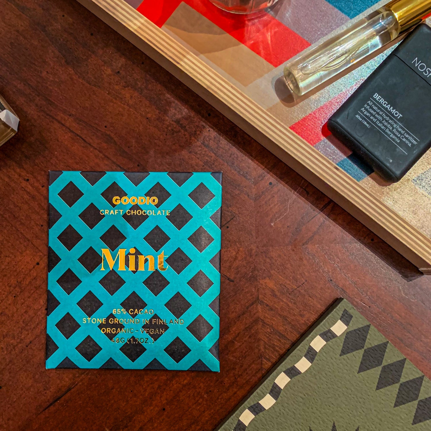 goodio chocolate mint packaging amongst other desk accessories. Packaging is a blue/green background with black diamond motif