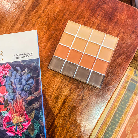 Subtle Art Studio’s “Ombré Copper” coaster with a brown to tan gradient. Sits on top of a side table with the corner of a book showing. The book says “A microhistory of heretical herbs”