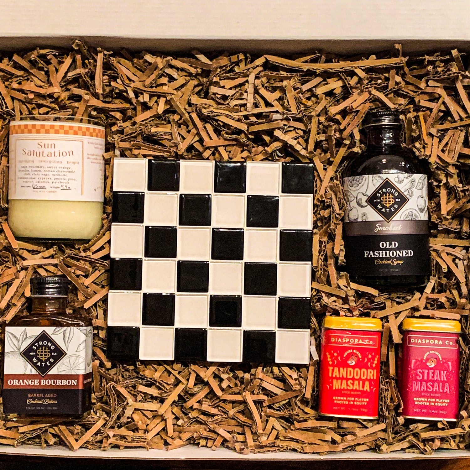 "Culinary Classics" housewarming gift box with a "sun salutation" soy wax candle, a square checkered trivet, smoked old fashioned syrup, orange bourbon bitters, and Diaspora Co.'s Tandoori Masala and Steak Masalas