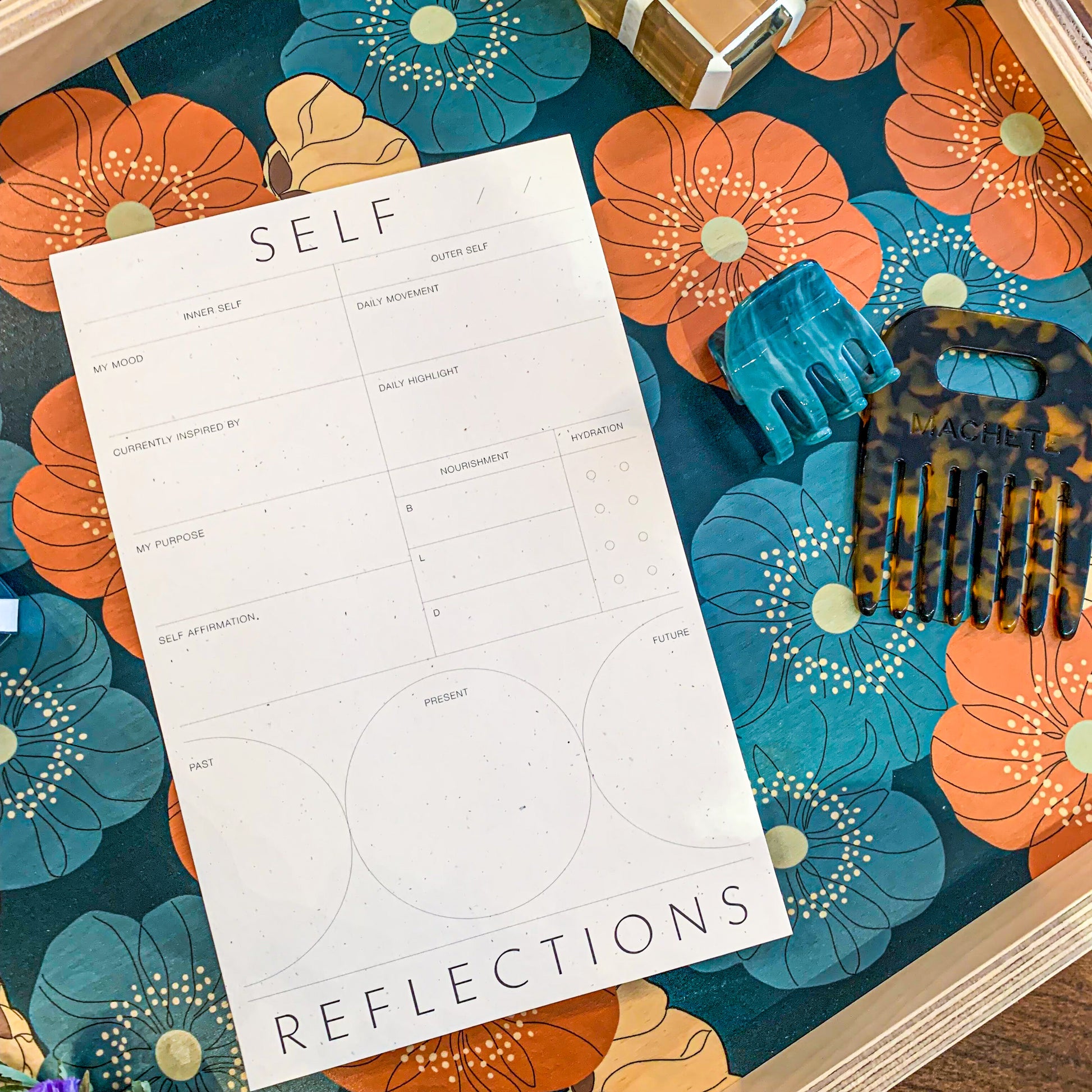 Wilde house paper “self reflections pad” on a blue and orange poppy decorative tray. There is also a Machete comb no 4 in classic tortoise on the right on the reflections pad.