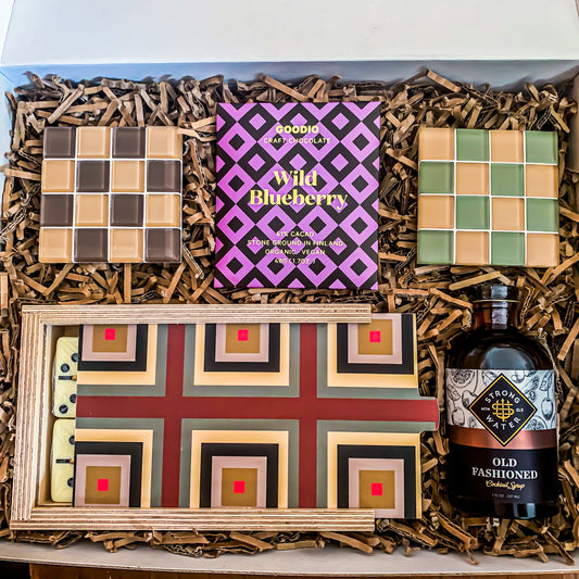 "Classic Shapes" High-End housewarming gift contains old fashioned syrup concentrate, a wooden domino set with a maroon square pattern, a pair of checkered glass tile coasters and vegan blueberry chocolate